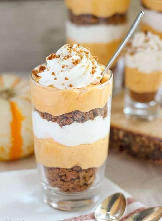 A small glass of pumpkin cream pie trifle topped with whipped cream and with a little spoon in it