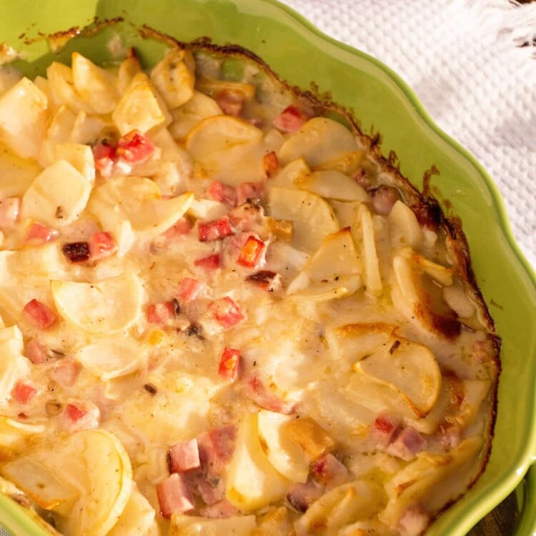 A green baking dish of scalloped potatoes sitting on a white towel