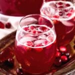 Two glasses of skinny spiced cranberry punch with cranberries and ice cubes in them sitting on a metal serving tray