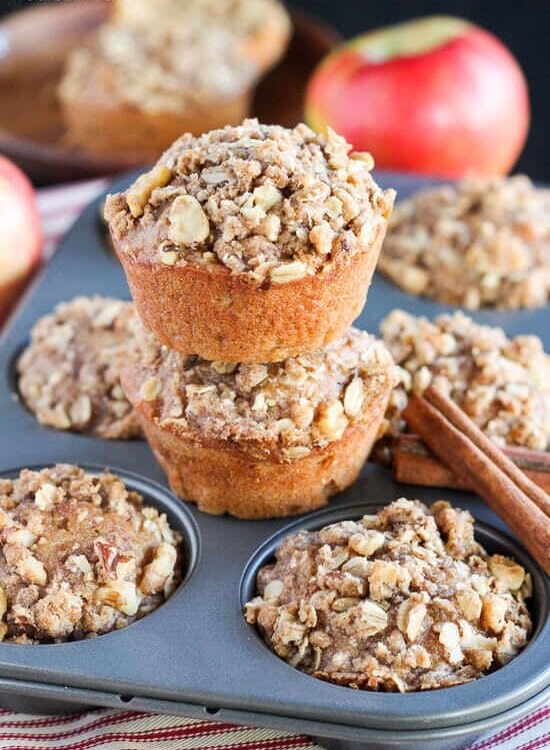 A six muffin tin of apple oat muffins with two more muffins stacked on top