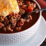 A white bowl of light crock pot spicy turkey chili with a spoon and topped with sour cream and shredded cheese