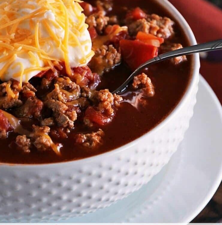A white bowl of light crock pot spicy turkey chili with a spoon and topped with sour cream and shredded cheese