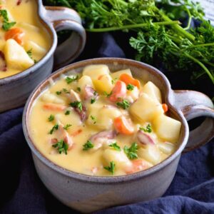 Two bowls of cheesy bacon potato soup on a navy kitchen towel with fresh parsley