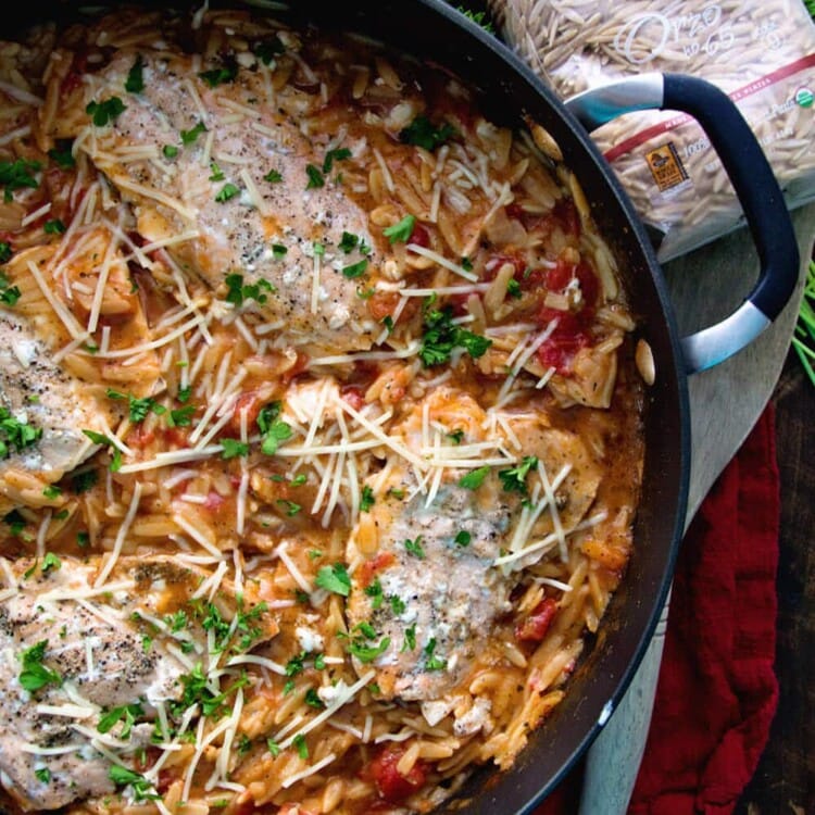 Skillet of light one pot Italian salmon and orzo next to a wooden spoon and a package of orzo