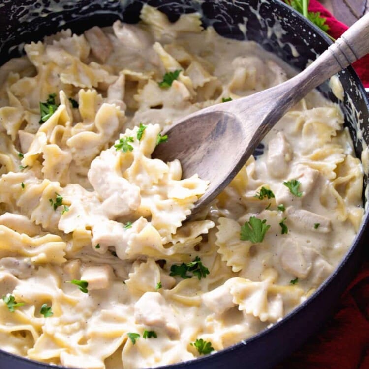 Skillet of one pot garlic chicken alfredo with a wooden spoon in it on a red kitchen towel