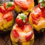 Overhead image of four stemless wine glasses of rainbow sangria containing slices of kiwi, pineapple, and strawberry