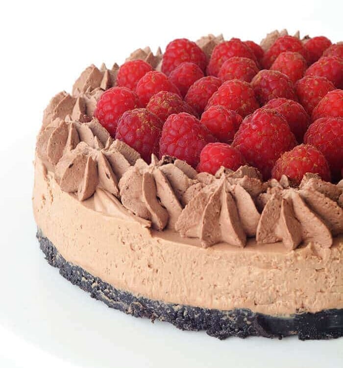 A raspberry chocolate cheesecake on a white cake stand