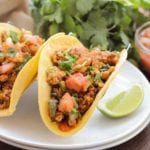 Two chorizo breakfast tacos on a white plate with lime wedges and parsley in the background