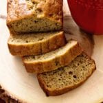 Partially sliced loaf of healthy banana bread next to a red mug of coffee on a wood tray