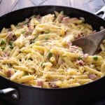 Skillet pan of one pot ham and penne pasta with a wooden spoon in it