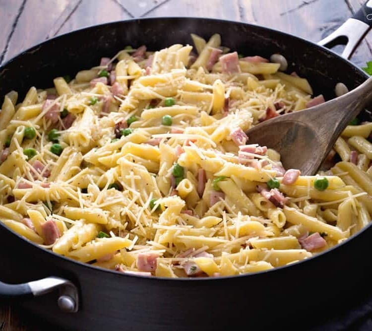 Skillet pan of one pot ham and penne pasta with a wooden spoon in it