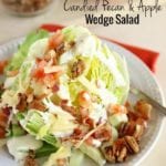 Candied pecan and apple wedge salad with dressing on a white plate with a fork sitting on a red napkin