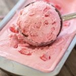 Strawberry ice cream being scooped out of a metal loaf pan