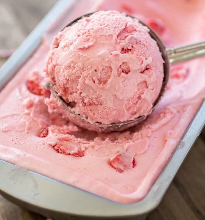 Strawberry ice cream being scooped out of a metal loaf pan