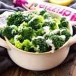 A cream bowl of easy garlic parmesan broccoli on a table next to a bottle of drizzle garlic parmesan sauce