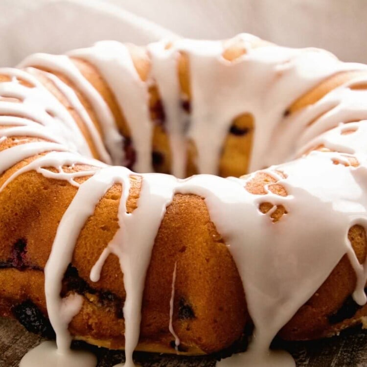A fresh blueberry coffee cake ring with icing on top sitting on a wood table