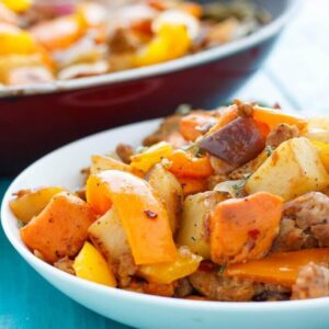 A shallow white bowl of sweet potato has with peppers and onions on a blue table