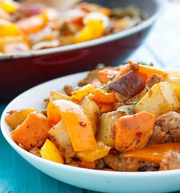 A shallow white bowl of sweet potato has with peppers and onions on a blue table