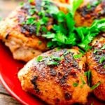 Seasoned and grilled chicken breasts on a red plate with fresh parsley garnish
