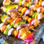 A hand holding a chipotle chicken kabob over a pan of grilled kabobs