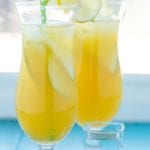 Two glasses of pineapple fruit cocktail with lemon slices on the rim