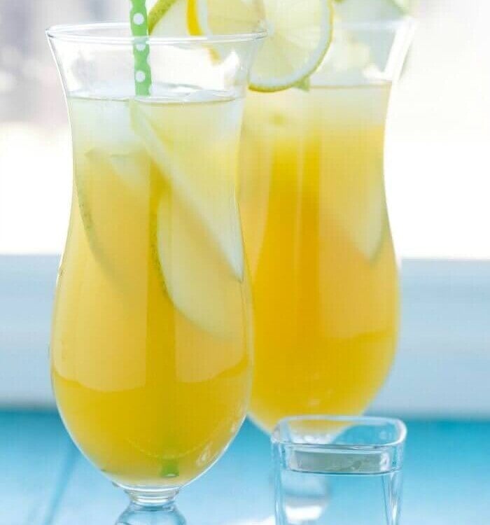 Two glasses of pineapple fruit cocktail with lemon slices on the rim