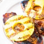 Two grilled pork chops topped with grilled pineapple on a white plate