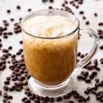 A clear glass mug on a counter covered in coffee beans