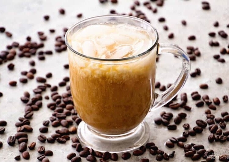 A clear glass mug on a counter covered in coffee beans