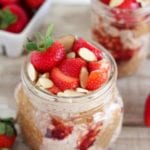 Two clear glass jars of strawberry almond overnight oats on a table with fresh strawberries on it