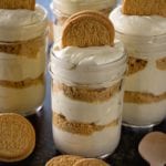 Four mason jars of Oreo dream salad on a counter with golden Oreos and small wooden spoons