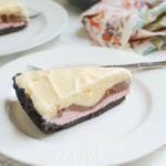 A slice of ice cream pie on a white plate with a fork in front of a glass pie plate containing the rest of the pie