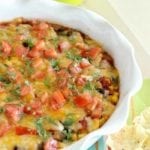 A white pie plate of southwestern bean cheese dip on a colorful cloth napkin with corn chips