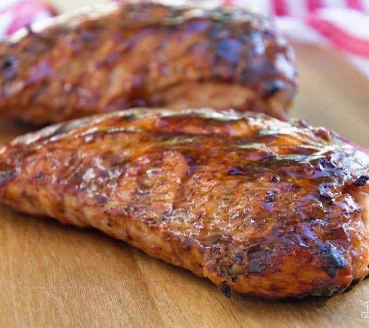 Two grilled bbq turkey loins on a wood cutting board