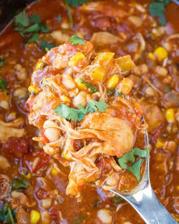 Overhead image of a large silver spoon scooping spanish chicken out of a crock pot