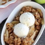 A white bowl of apple pear crisp topped with two scoops of vanilla ice cream