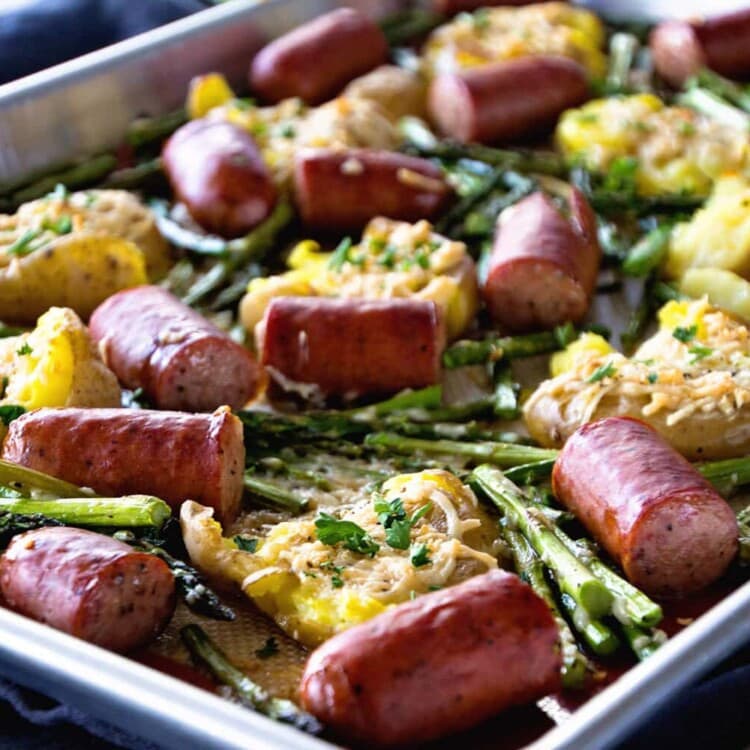 A metal sheet pan of sausage, smashed potatoes, and asparagus