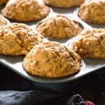 A muffin tin of skinny peanut butter banana muffins sitting on a kitchen towel along with berries