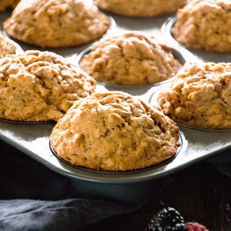 A muffin tin of skinny peanut butter banana muffins sitting on a kitchen towel along with berries
