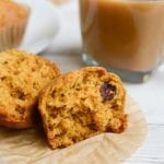 A pumpkin cranberry muffin ripped in half on a cupcake liner next to a glass of coffee