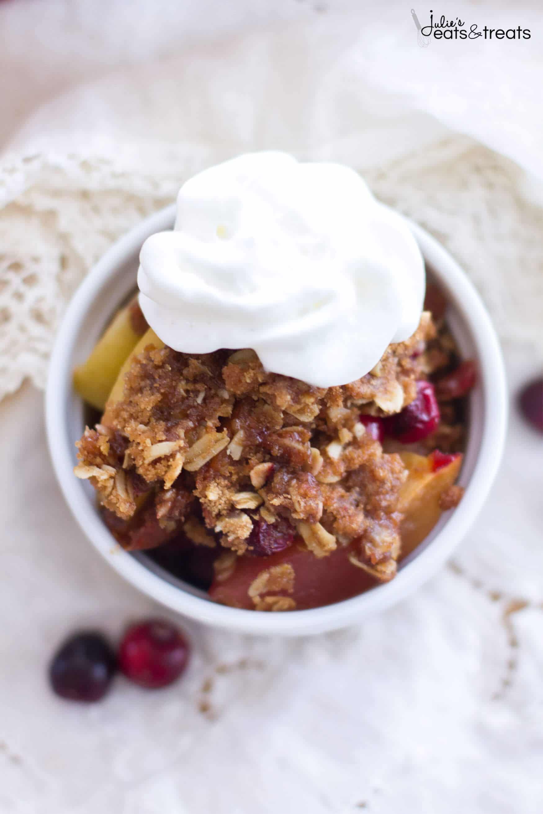 An overheat shot of Apple Cranberry Crisp in a white bowl topped with a dollop of whipped cream.