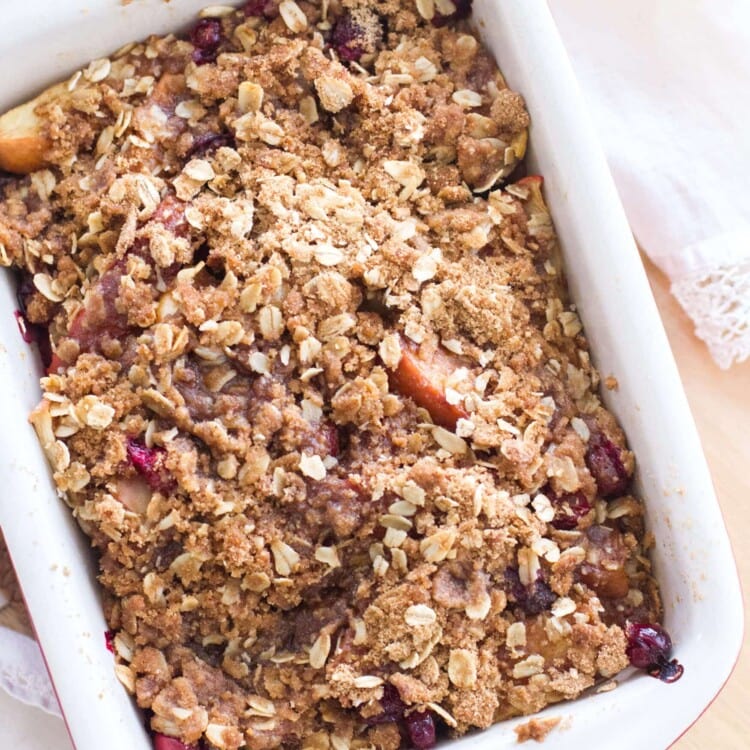 A white rectangular baking dish of apple cranberry crisp on a wood table