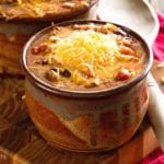 Two brown bowls of famous chili with shredded cheese on top sitting on a wood cutting board