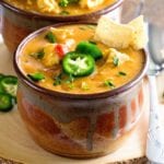 Two brown bowls of king ranch chicken soup on a wood stump with jalapenos and a spoon