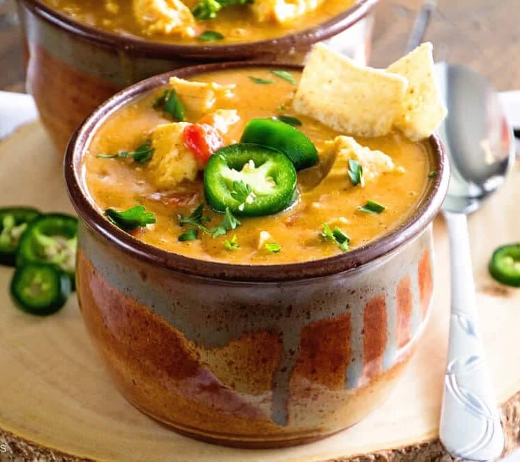 Two brown bowls of king ranch chicken soup on a wood stump with jalapenos and a spoon