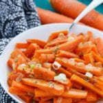 A white bowl of slow cooker ranch carrots on a blue table with a cloth napkin and three carrots