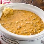 A white crock pot of spicy crock pot hamburger dip with a chip in it