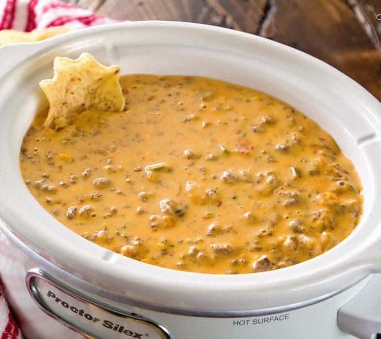A white crock pot of spicy crock pot hamburger dip with a chip in it