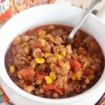 A white bowl of black eyed pea sausage chili with a spoon in it