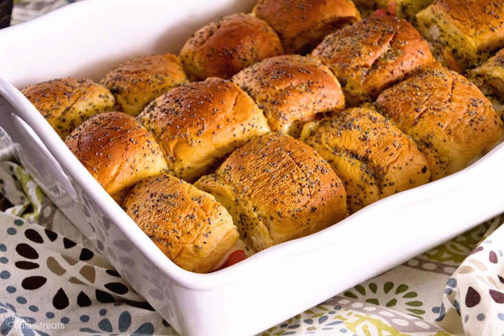 White casserole dish with turkey sliders topped with poppy seeds in them.